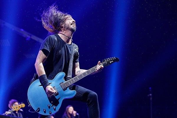 Dave Grohl of Foo Fighters performing amid a blue background and bright blue lights during a show in Detroit, Michigan.