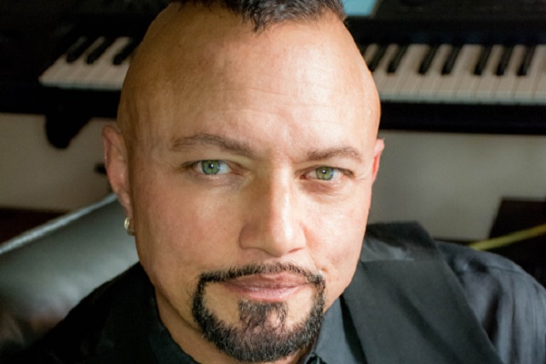 Geoff Tate sits in his studio in front of a black and white keyboard.