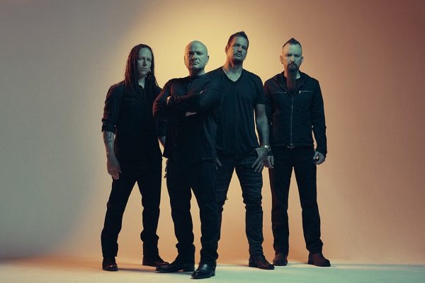 The members of Disturbed standing against a dimly lit background.