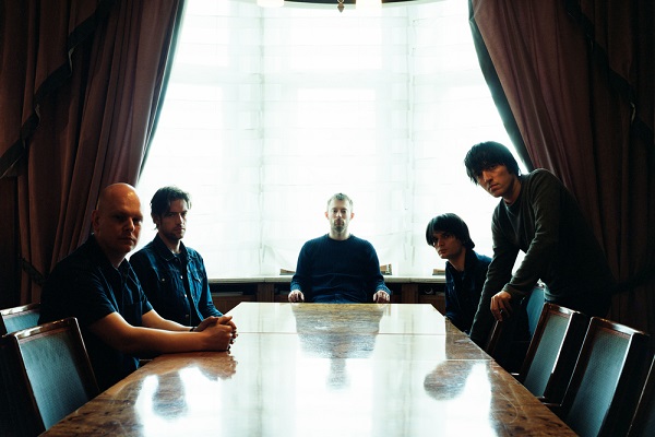 The members of Radiohead sitting at the end of a long table.