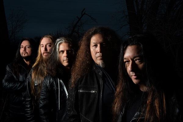 Promo photo of thrash metal band Testament standing amid a dark background.