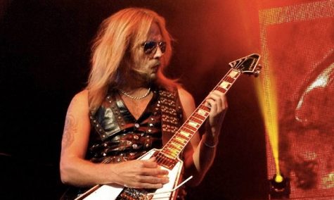 Photo of RIchie Faulkner of Judas Priest performing live amid red and yellow lighting.