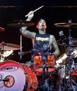 Travis Barker of Blink-182 performing live, rocking out on a red and white drum kit.