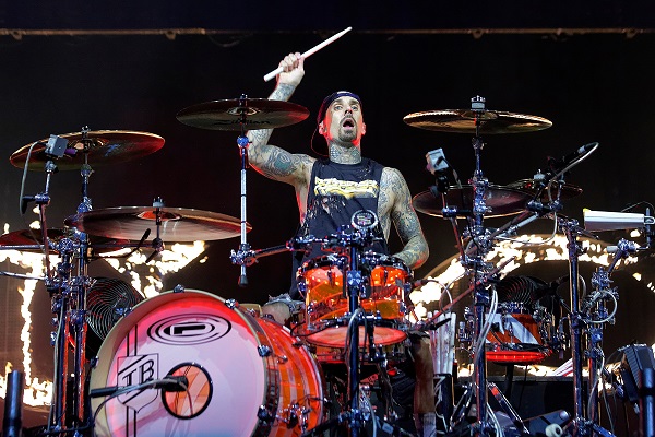 Travis Barker of Blink-182 performing live, rocking out on a red and white drum kit.