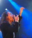 Incubus frontman Brandon Boyd performing live in Detroit, Michigan, amid a blue background.