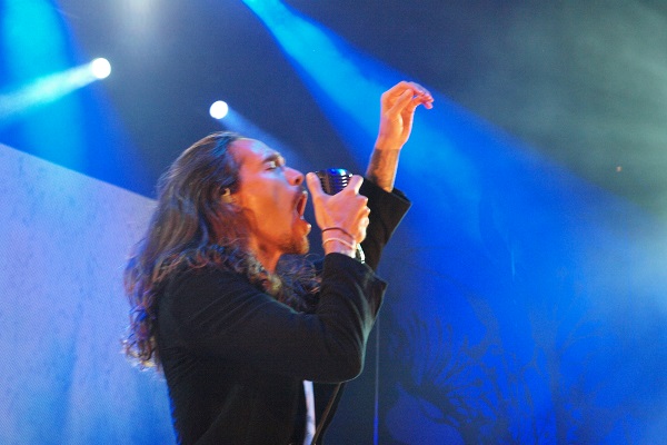 Incubus frontman Brandon Boyd performing live in Detroit, Michigan, amid a blue background.