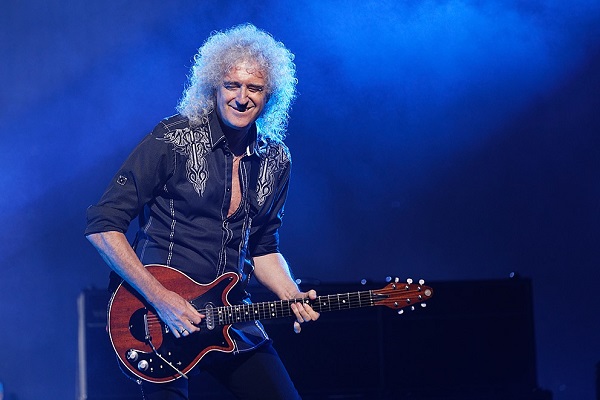 Brian May of Queen performing live amid a bright blue background. May pays tribute to late Animals guitarist Hilton Valentine with two videos in which he plays "House of the Rising Sun."