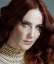 Epica vocalist Simone Simons posting with a beige collard shirt and bright, blue eyes. Epica's new album is 2021's "Omega."