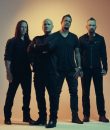 The members of Disturbed standing against a dimly lit background.