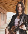 Myles Kennedy standing with an acoustic guitar.