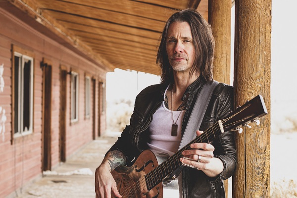 Myles Kennedy standing with an acoustic guitar.