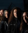 Promo photo of thrash metal band Testament standing amid a dark background.