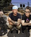 Outdoor image of the members of Blink-182 posing on a city street.