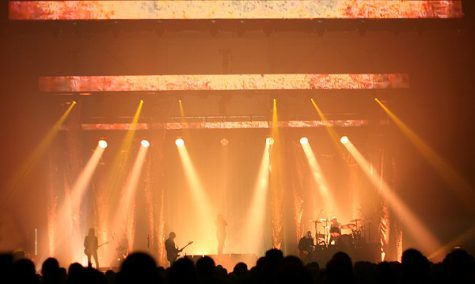 Image of a rock band performing live with orange and yellow lights.