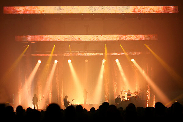 Image of a rock band performing live with orange and yellow lights.