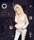 Image of Dolly Parton with ripped jeans standing against a black background.