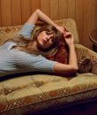Taylor Swift laying down on a brown couch.